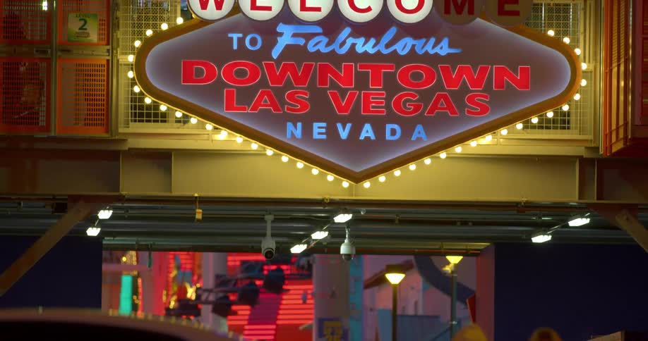A crowd of people walks under a welcome sign in las vegas