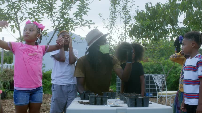 A man shows a group of young kids how to grow plants in containers