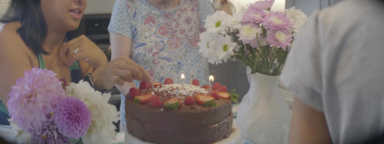 A young girl jumps up and down as her mother blows out candles on her birthday cake