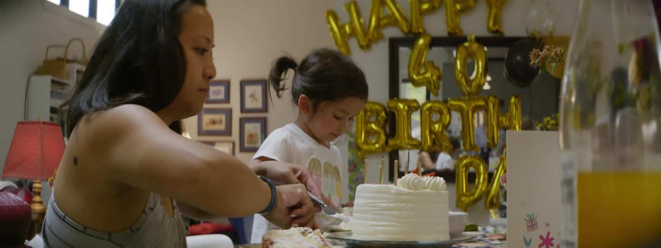 A mom and daughter prepare a birthday cake at a table