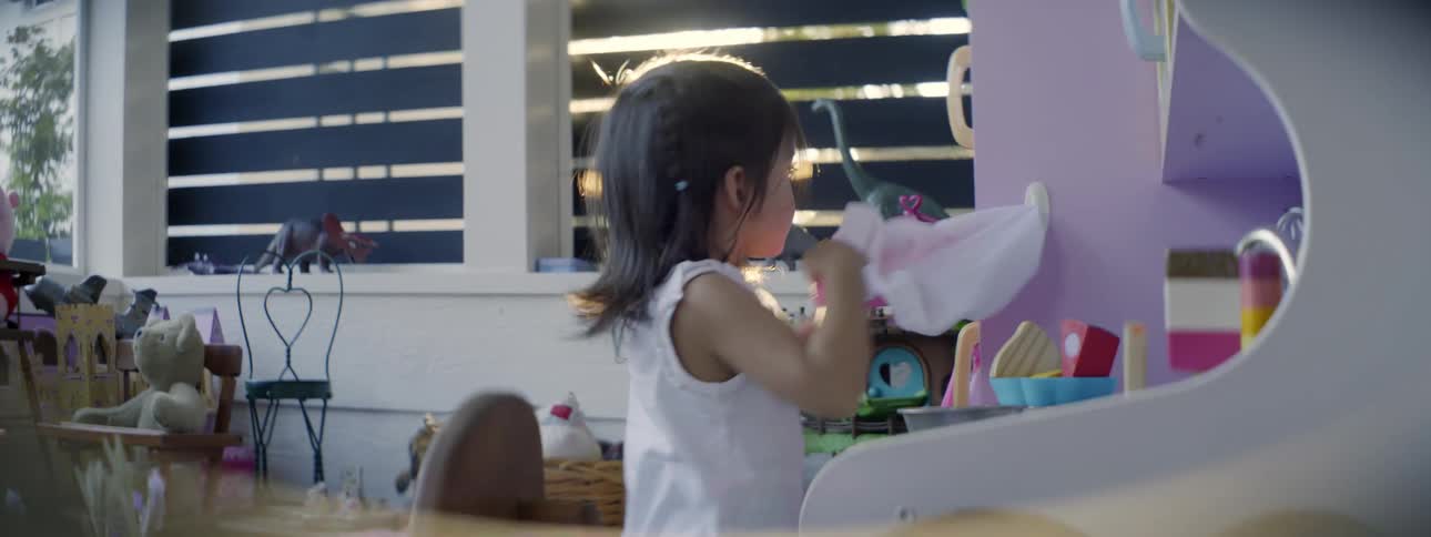 Little girl playing at a toy kitchen in her room on a sunny day