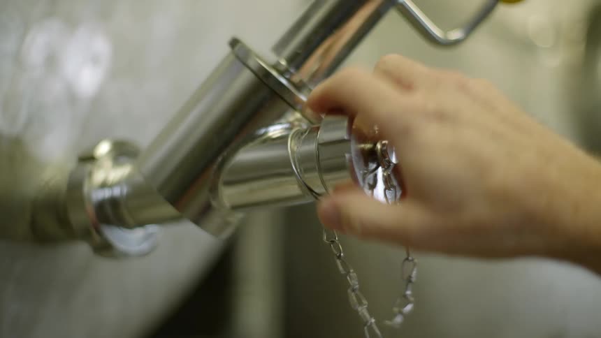 A person twists a cap onto the open end of a pipe attached to a tank