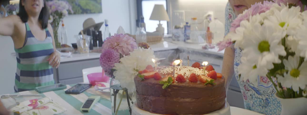 A girl and two women try to out candles on a cake