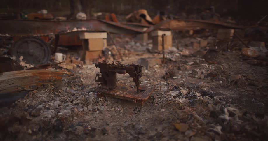 A discarded metal sewing machine sits in a dirt field with bricks and other trash