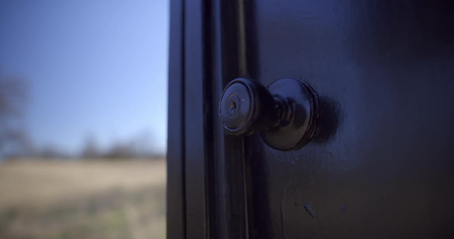 Door knob on door outside with grass and trees in the background