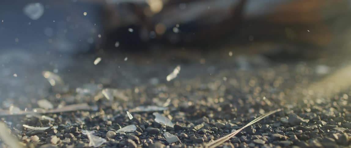 A glass bottle shatters and sends shards flying after it drops on gravel outdoors