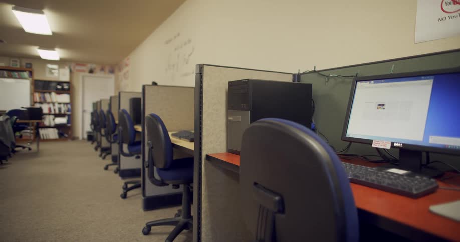 An empty computer classroom with a row of work stations with chairs and computers