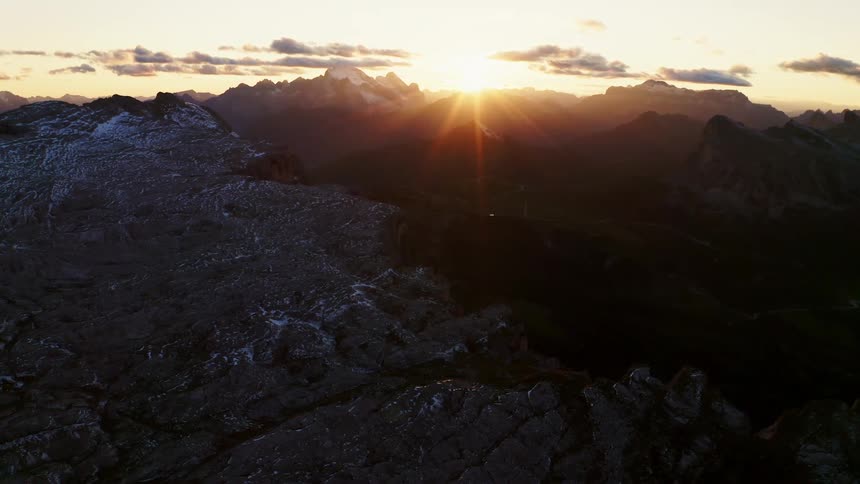Sun peaks over mountains shining across dark valley toward snow and ice covered slope