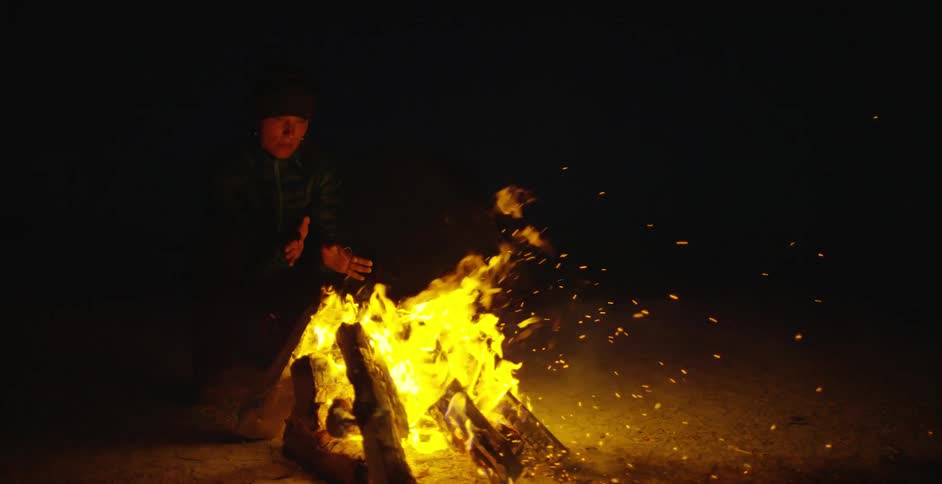 A person is warming near a campfire at night