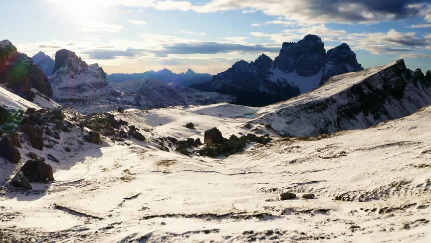 Snow covers the rocky surfaces of a mountain range beneath a beautiful sky