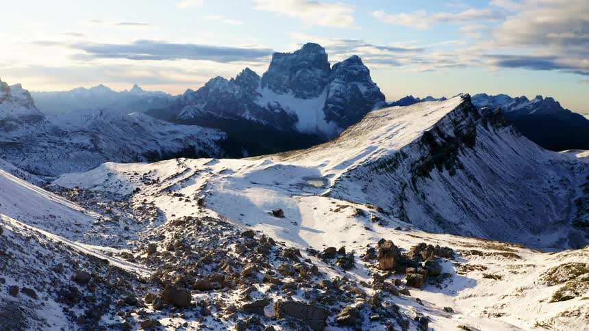 Mountains covered in snow with some rocks on a sunny day with blue sky and clouds above