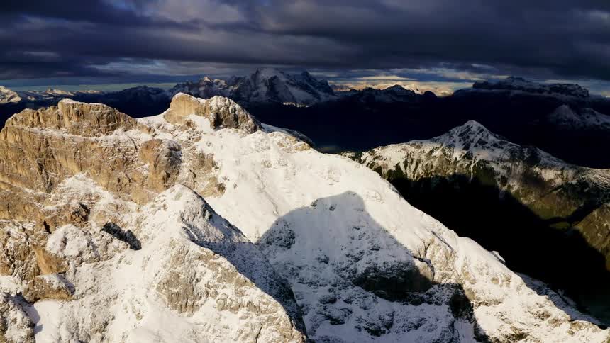 Dark clouds loom over a snow powdered mountain range in the evening