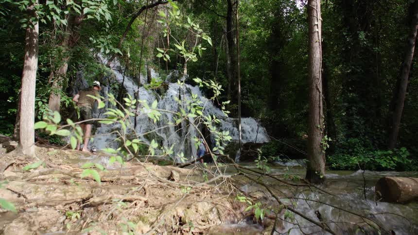 Two people explore a forest with a waterfall and stream