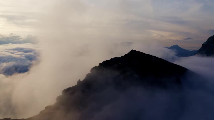 Mountain peak above the clouds with the sun in the background