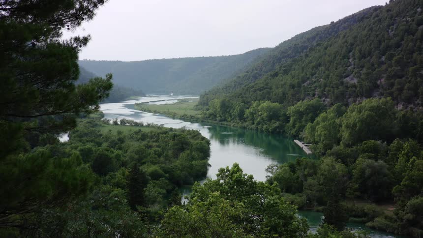 A river with hills with greenery and trees all around on a hazy day