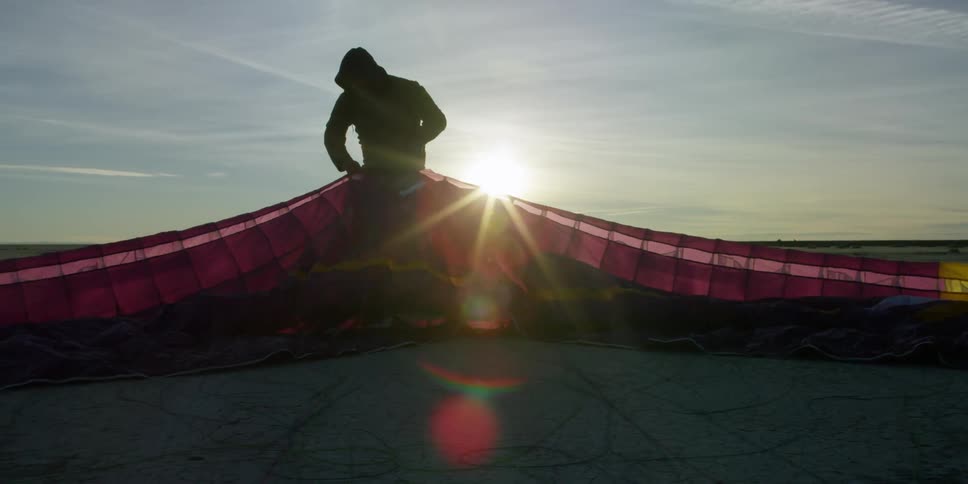 Man straightening out a large parasail as the sun sets