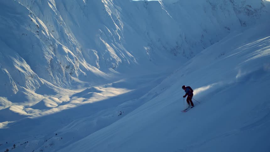 A person skis down a snowy mountain in the sun