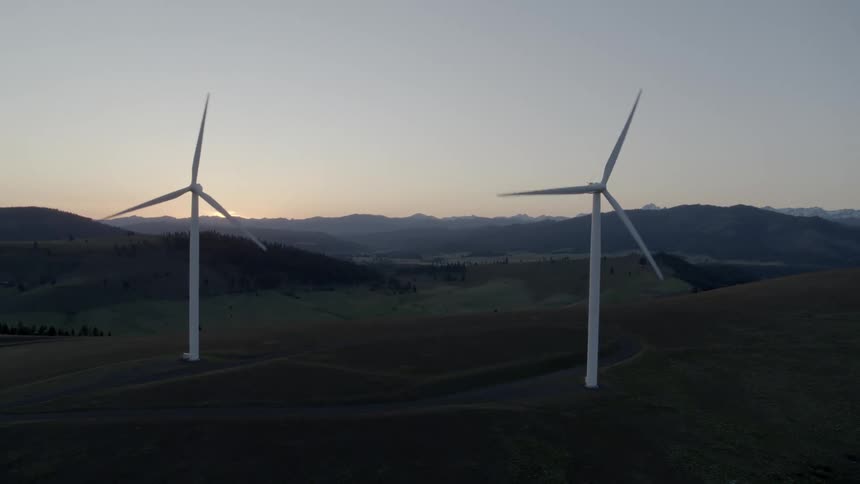 Clockwise orbit around two wind turbines on a wind farm at dusk