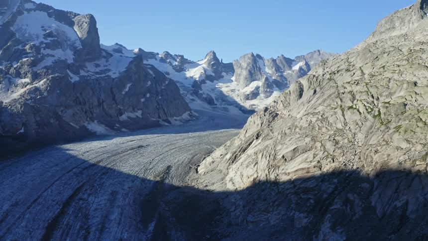 A cleared road in the middle of a mountain range with snow on a clear day