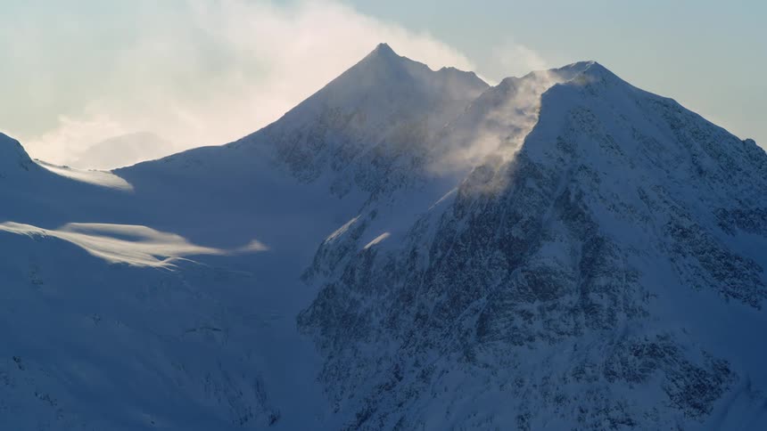 Wind blows the snow off a mountain top