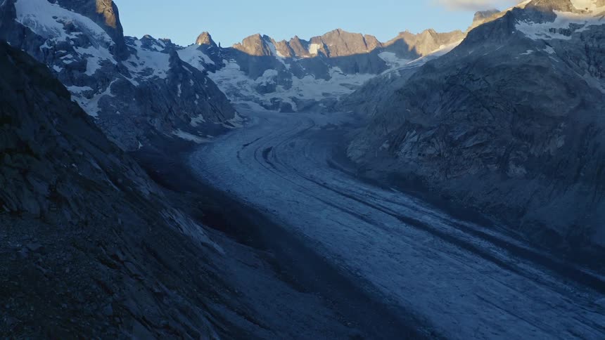 Icy road through mountain pass heads in to the distance where sunlight can be seen at mountain tops