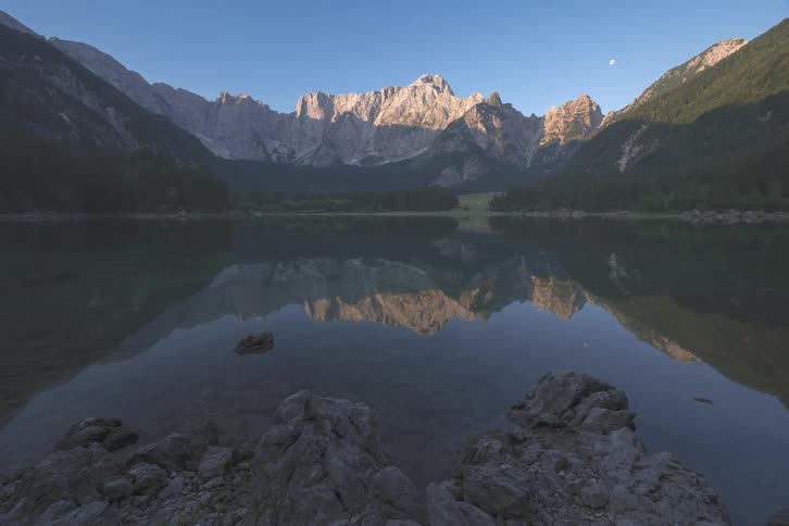 The moon rising above the mountains next to a lake