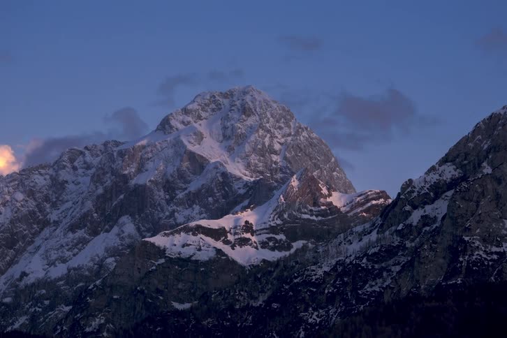 Dense clouds float past a mountain range as day turns to dusk