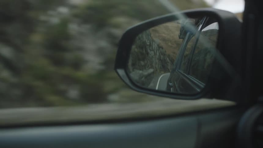 Car drives past foot of rocky mountain covered in dried grass