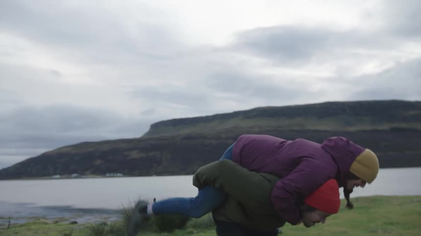A couple running outside and a woman getting a piggyback ride near a lake
