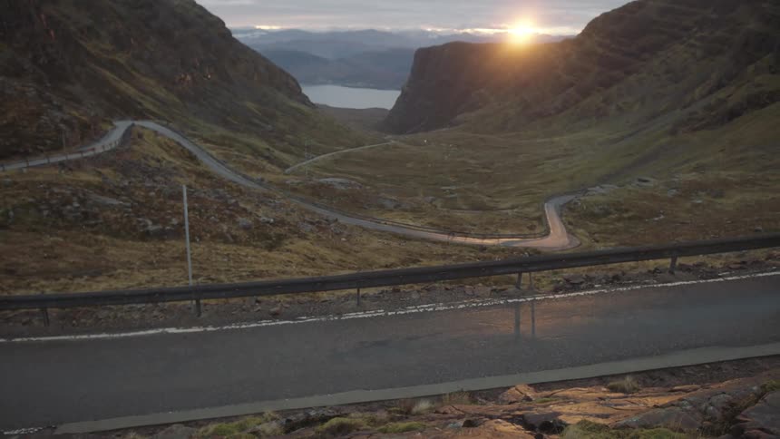 Sun sets over a road between mountains