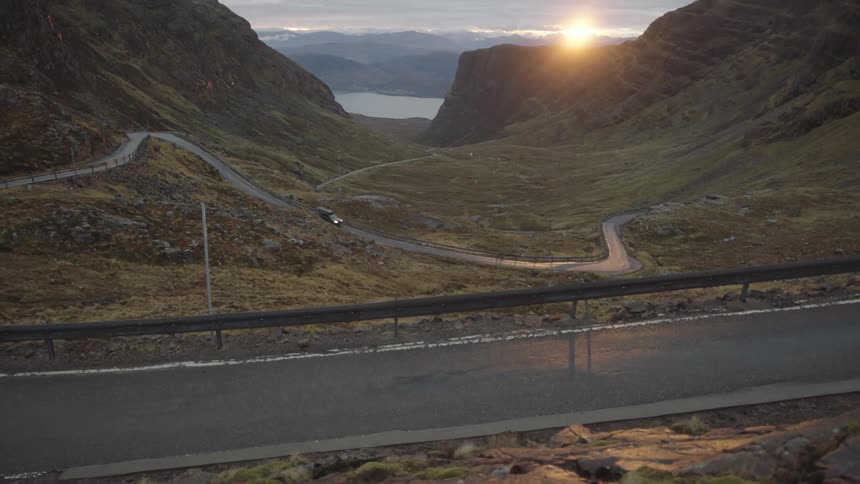 A trucks drives along a winding mountain road as the sun hangs low in the sky