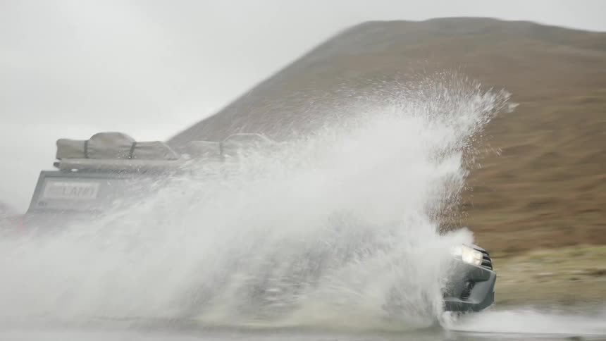 A trucks with equipment attached to the roof drives across a shallow stream