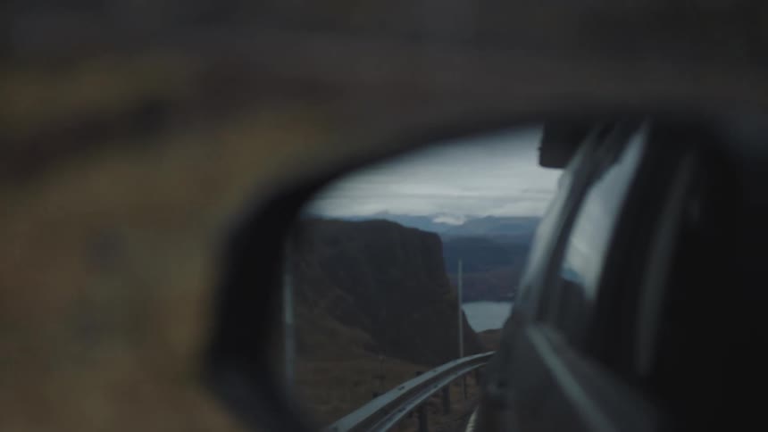 A car drives on a road with a mountain and road reflected in the side mirror of the vehicle