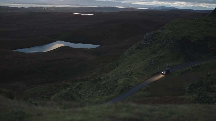 A car drive with headlights on through the hills on a road in the evening