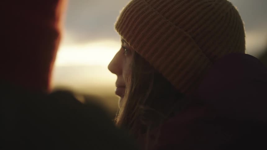 Woman standing next to someone looking off at a sunset