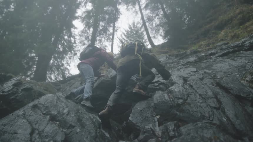 Two people are climbing a steep rock face of a mountain