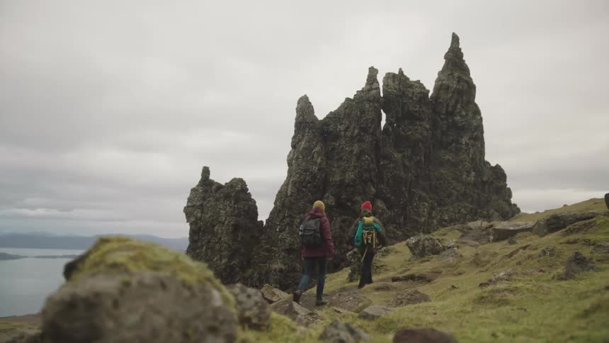 Man and a woman walking up a rocky mountain slope at day time next to a large body of water