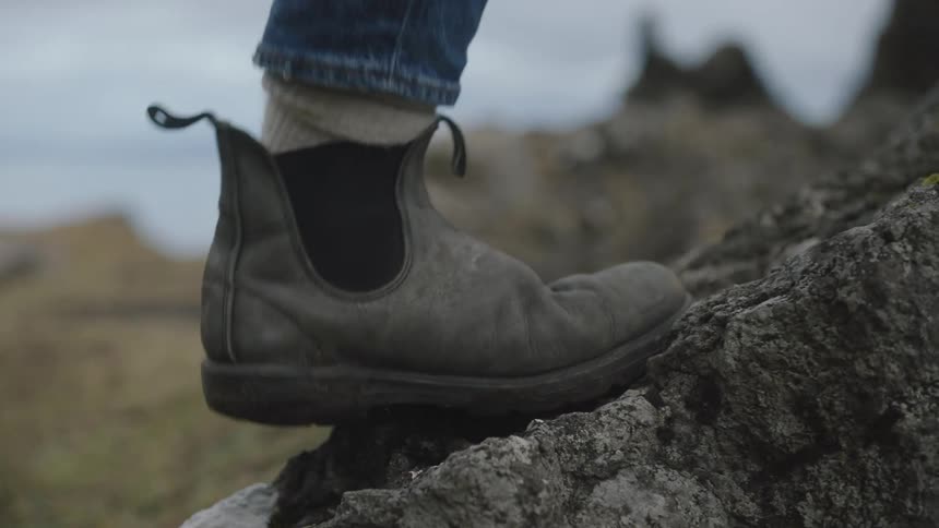 A close up of someones feet walking uphill with hills and a grey sky in the background