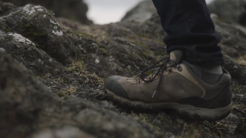 Foot wearing sneakers at day time climbing up a small rocky slope