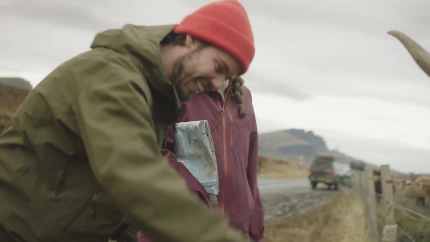 A man and woman stand by the side of the road and hand feed a highland cow