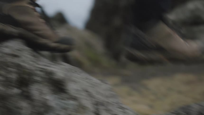 A person wearing boots swiftly hikes over rocky terrain