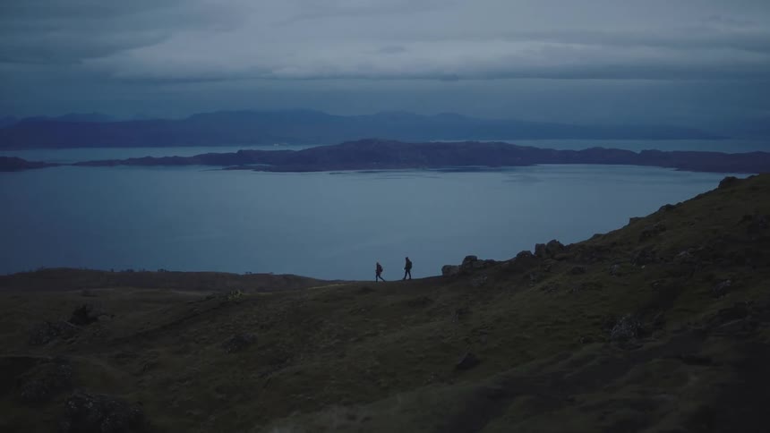 Two people walk down a hill next to a lake while using a flashlight