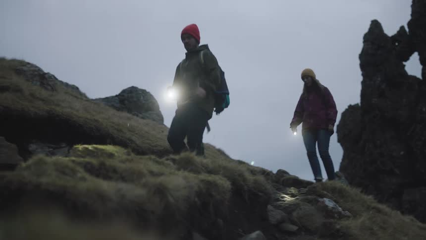 A man and woman walk over a rocky hill at night with a flashlight