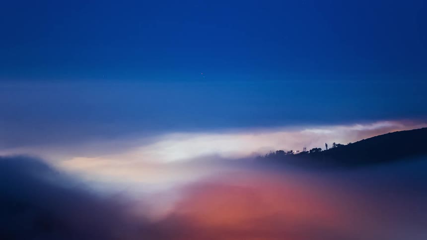 Fog flowing across landscape obscuring buildings and slope brightens as sun rises