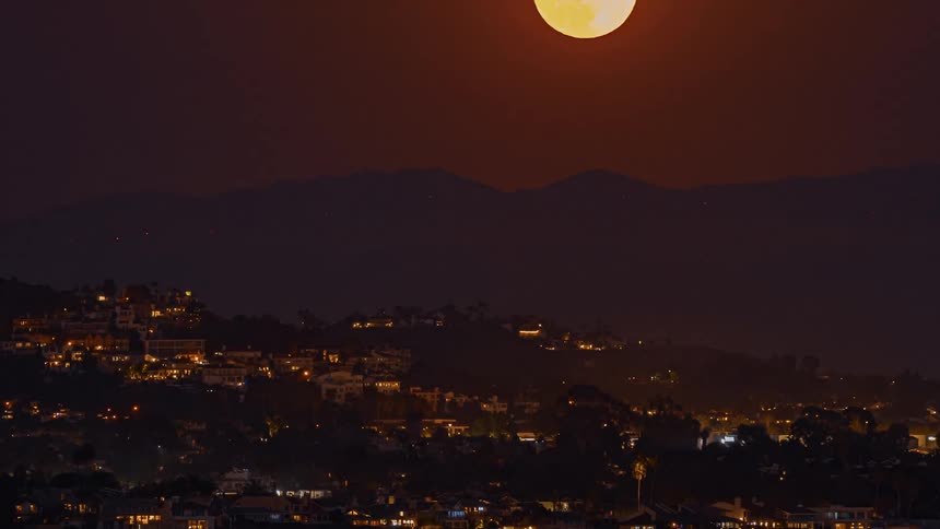 Time lapse of a full moon rising in the night sky above a city