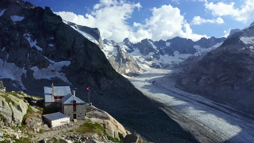 A building on a cliff overlooking the icy valley of a snow speckled mountain range during the day
