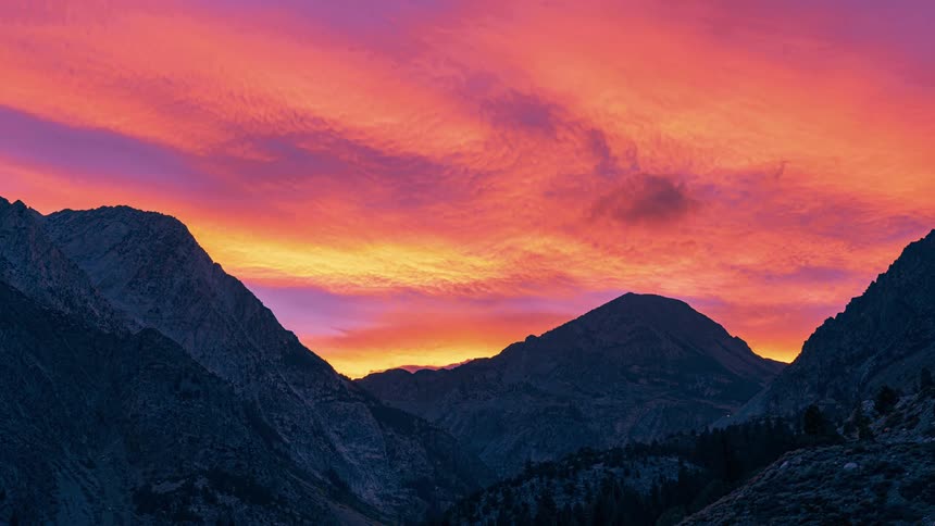 Clouds move across bright sky at sunset above mountain range