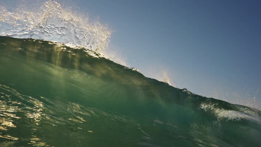 Huge wave overcomes the view of the sun on a clear day