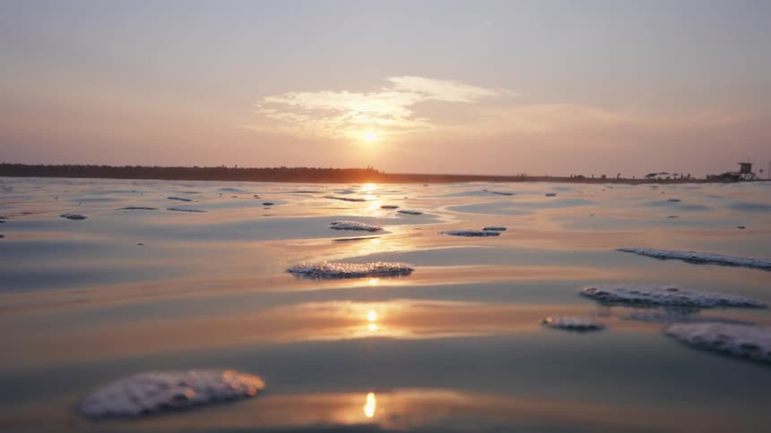 Surface of a body of water with land in the background with a setting sun