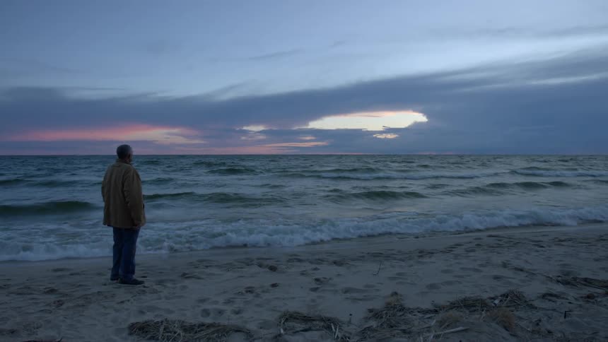 Man standing on a beach at sunset watching the waves next to the ocean